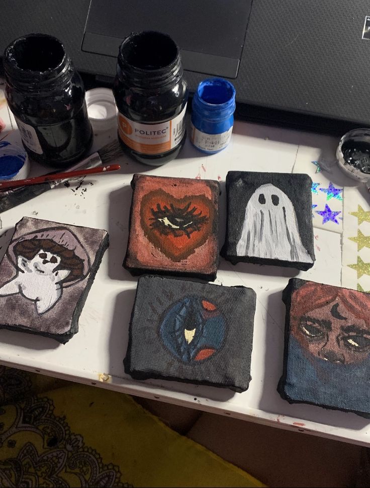 four small square coasters are sitting on a table next to some paint and brushes