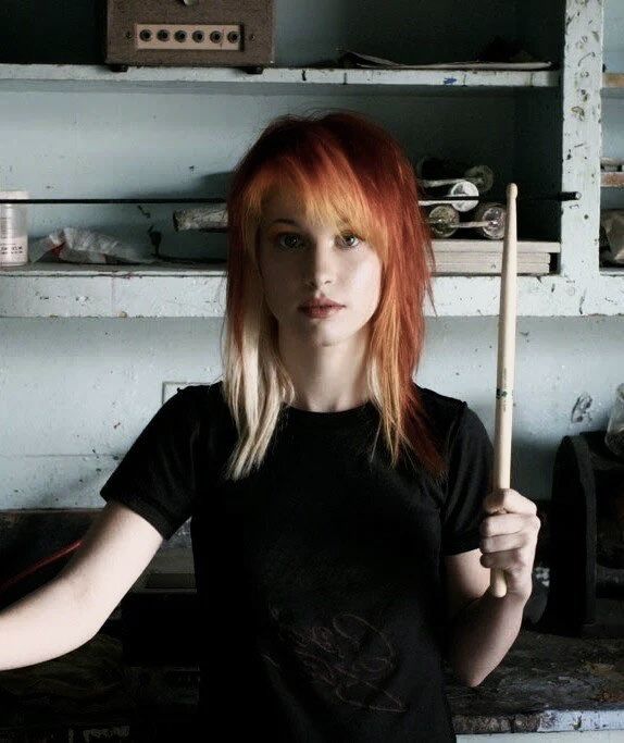 a woman with orange hair holding a wooden stick