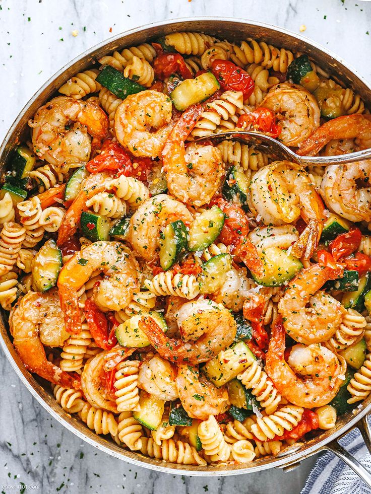 pasta with shrimp, zucchini and tomato sauce in a skillet on a white surface