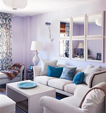 a living room with purple walls and white couches in front of a mirror on the wall