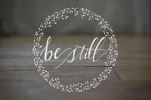 the word be still is written in a circle with leaves around it on a wooden surface