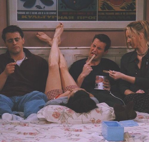 three people sitting on a bed with their feet up and one person holding a can