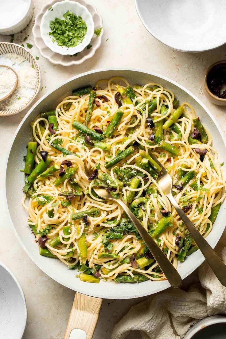 pasta with asparagus and olives in a white bowl on top of a table