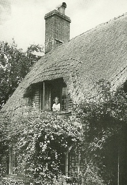 an old black and white photo of a woman in the window of a thatched house