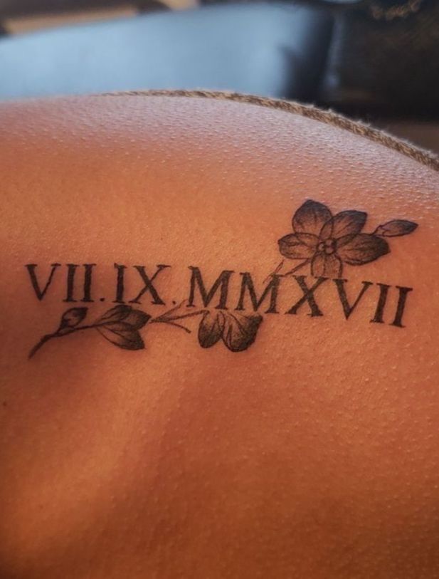 the back of a woman's shoulder with roman numerals and flowers on it