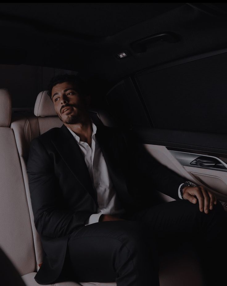 a man sitting in the back seat of a car wearing a black suit and white shirt