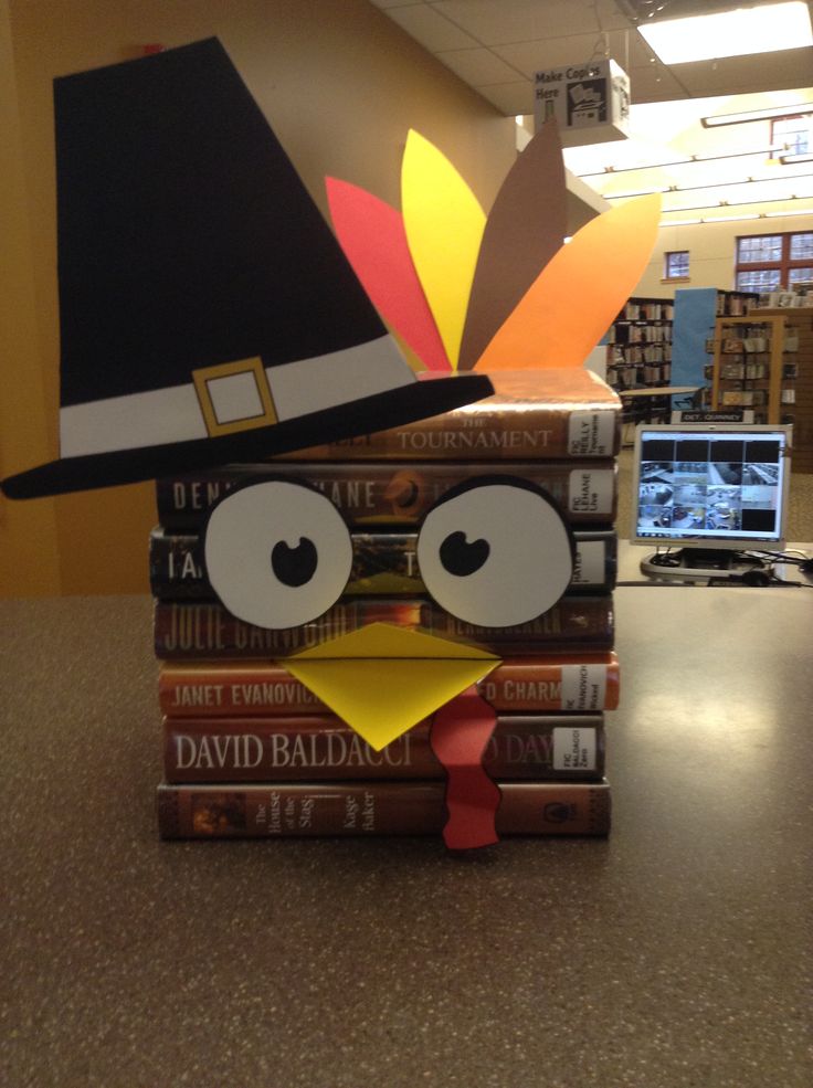 a stack of books sitting on top of a table next to a turkey head wearing a hat