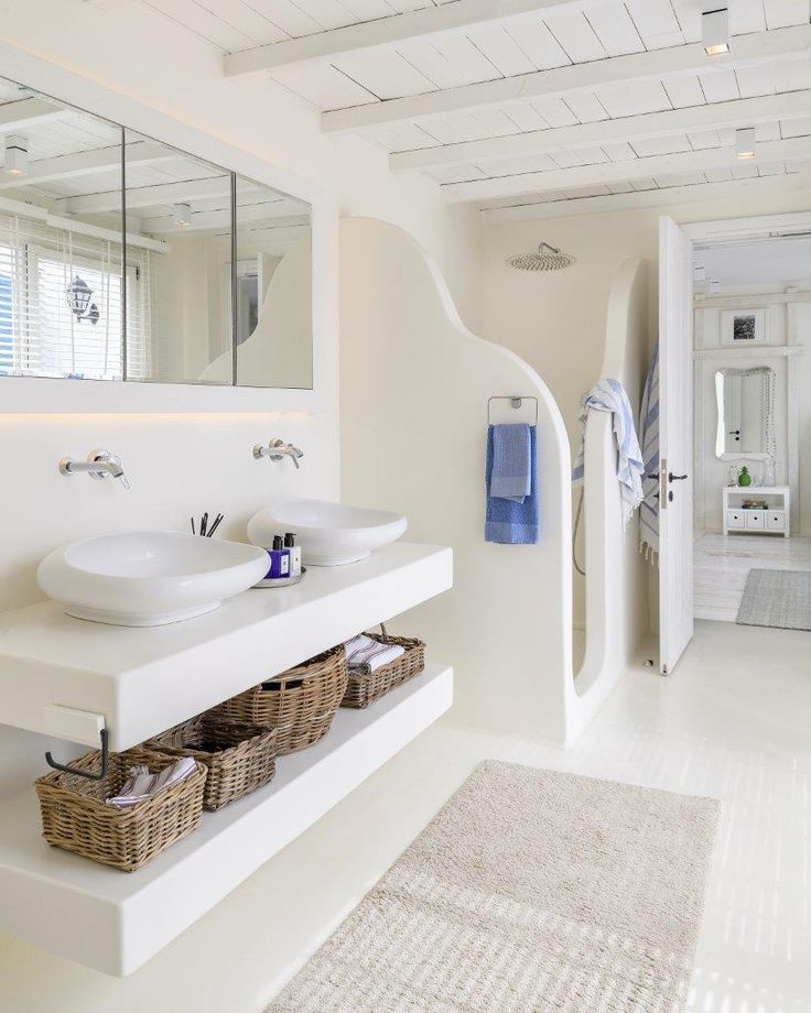 a white bathroom with two sinks, mirrors and baskets on the shelf next to it