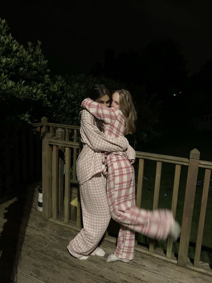 two women in pajamas hugging on a deck at night with their arms around each other