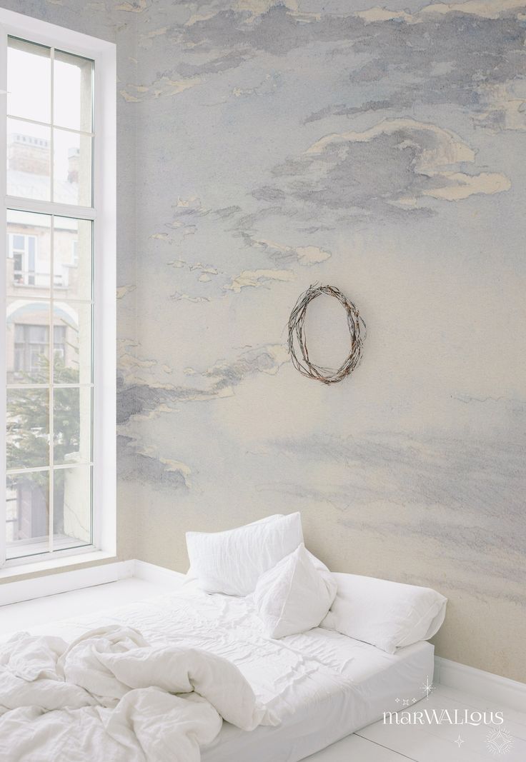 a white bed sitting under a window next to a wall with clouds painted on it