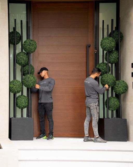 two men standing in front of a door with topiary balls on the doorsill