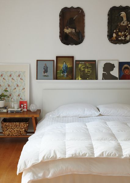 a white bed sitting in a bedroom next to two pictures on the wall above it