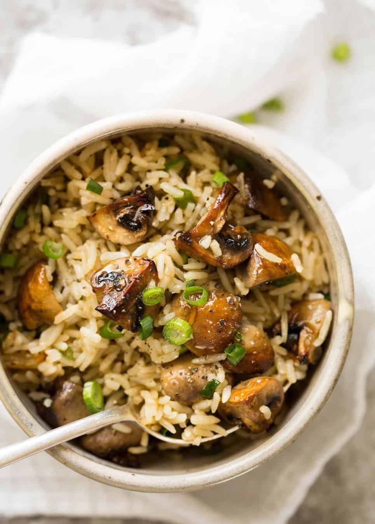 a bowl filled with rice and mushrooms on top of a white napkin next to a spoon