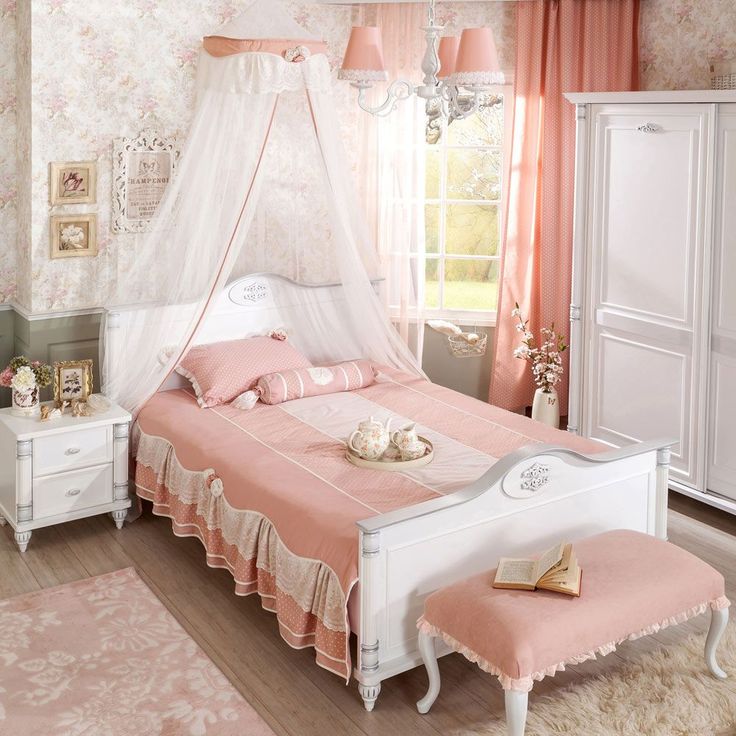 a white bed sitting in a bedroom next to a dresser and window with pink curtains