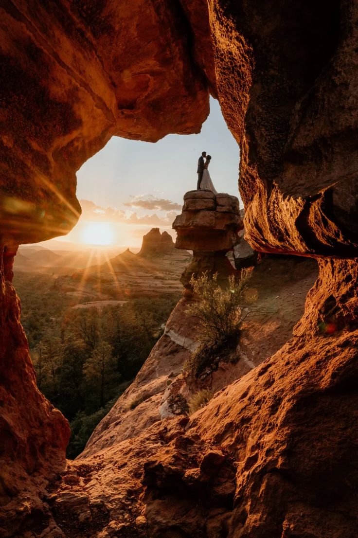 a person standing on top of a cliff with the sun setting in the distance behind them