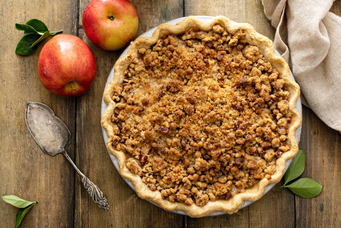 an apple pie on a wooden table next to two apples