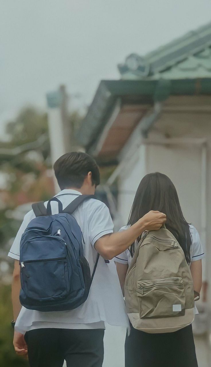 two people walking down the street with backpacks on their back and one person carrying a book bag