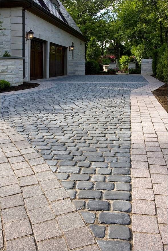 a driveway with cobblestones and trees in the background