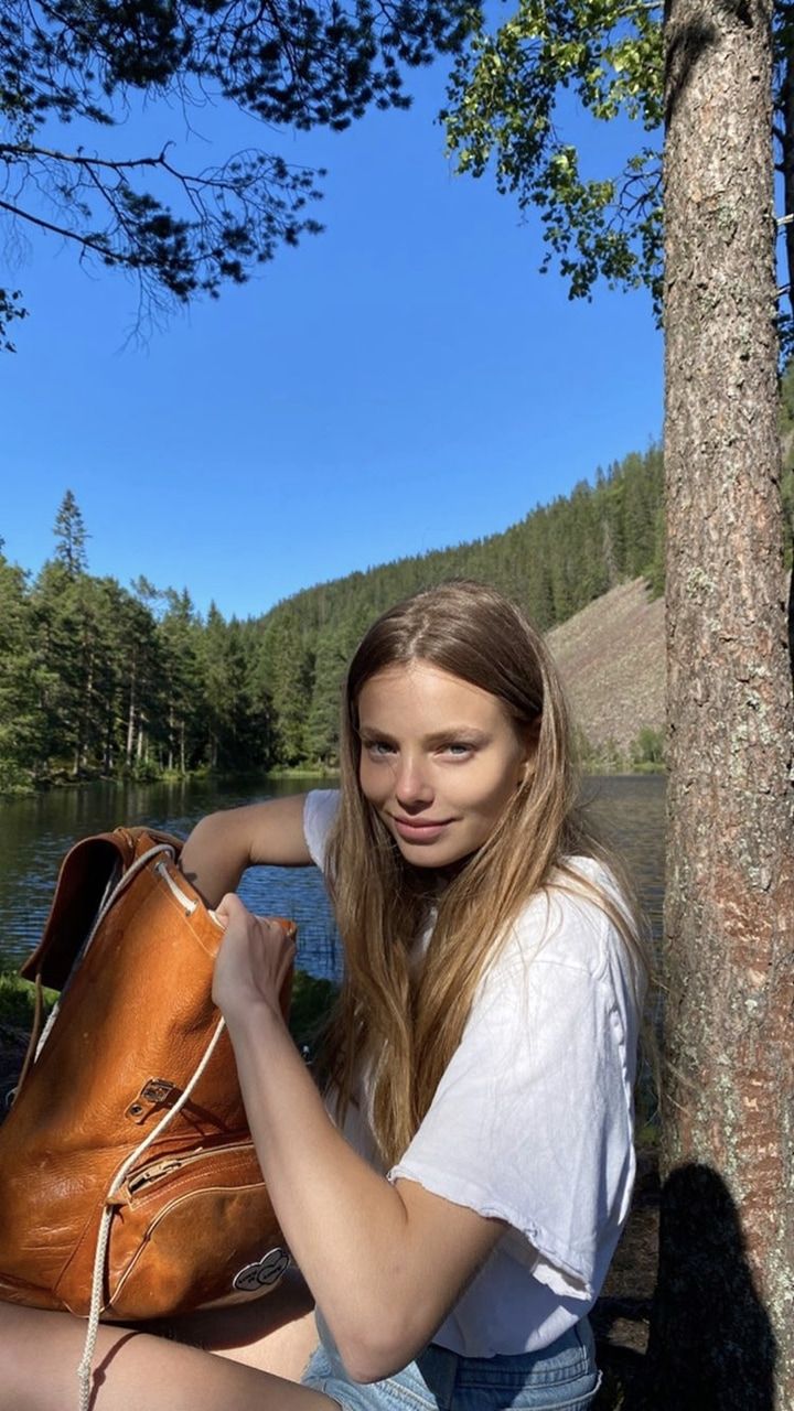 a woman sitting next to a tree holding a purse