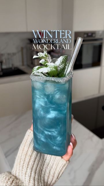 a woman holding up a blue drink in her hand with the words winter wonderland mock cocktail