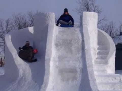 two snowboarders are sitting on the edge of an ice - covered wall and one is sliding down it