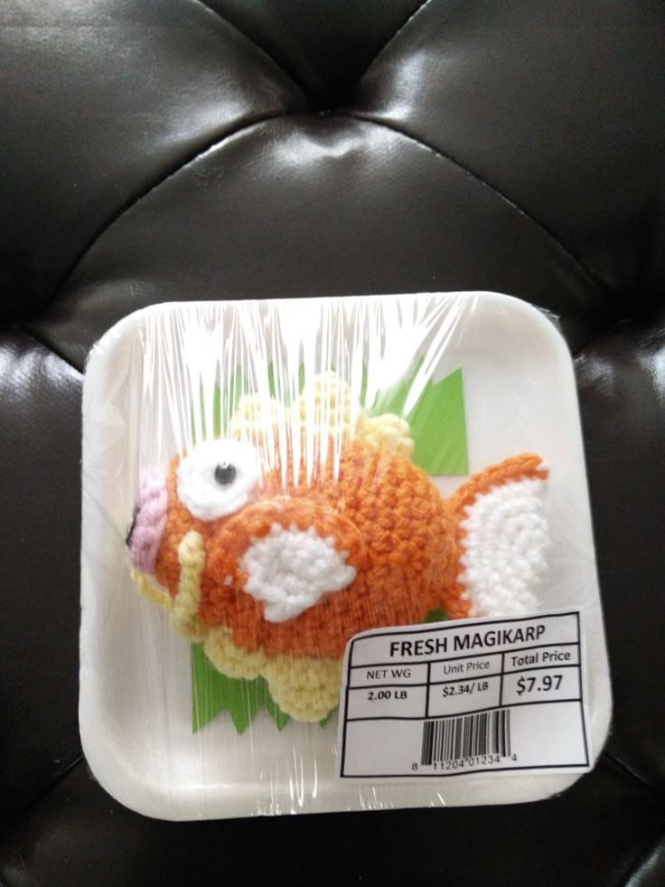 a plastic tray with a crocheted orange fish on it's side and the label says fresh magkap