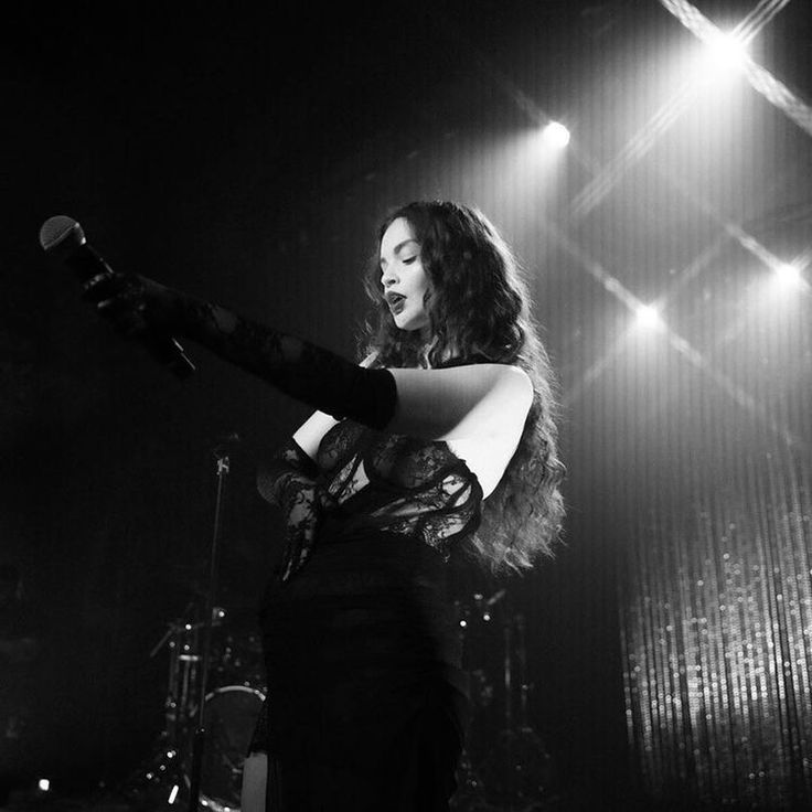 a woman standing in front of a microphone on stage with her arm extended and legs spread out