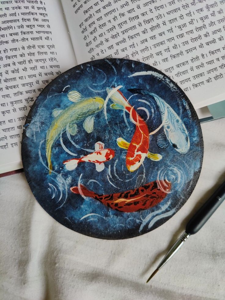 a plate with two koi fish on it next to a pen and an open book