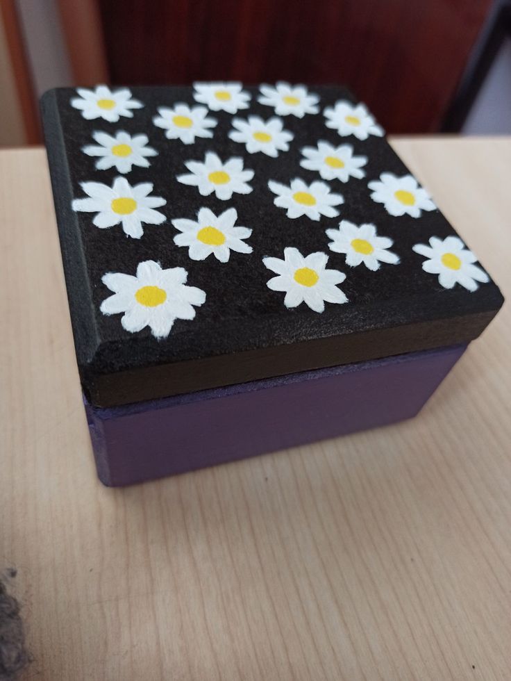 a black box with white and yellow flowers painted on the inside is sitting on a table