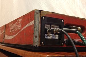 an old coca - cola box sitting on top of a wooden table next to a power cord