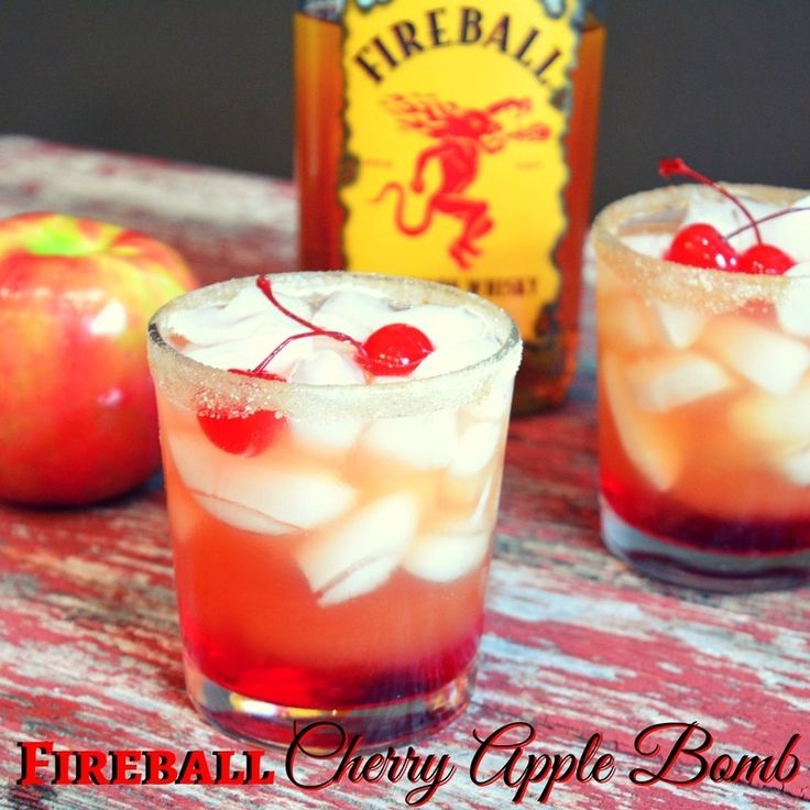 two glasses filled with ice and cherries on top of a table next to an apple