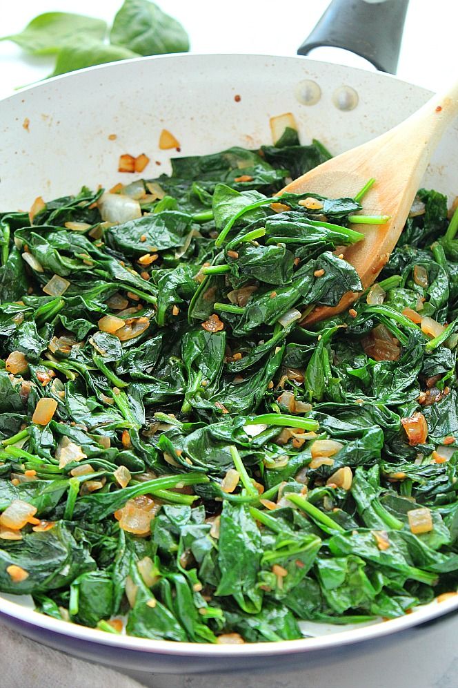 spinach and pine nuts are being cooked in a skillet with a wooden spoon