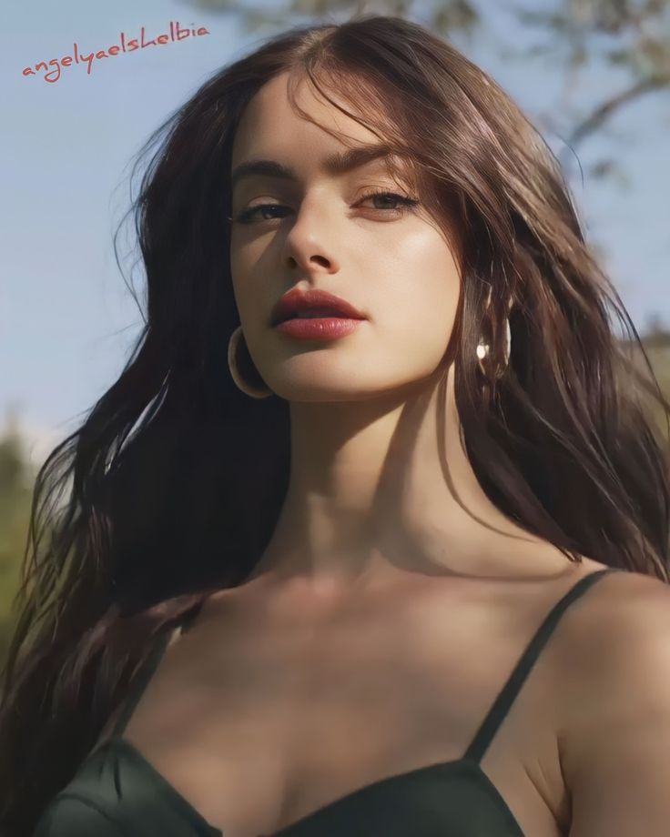 a woman with long brown hair wearing large hoop earrings and green dress looking off into the distance