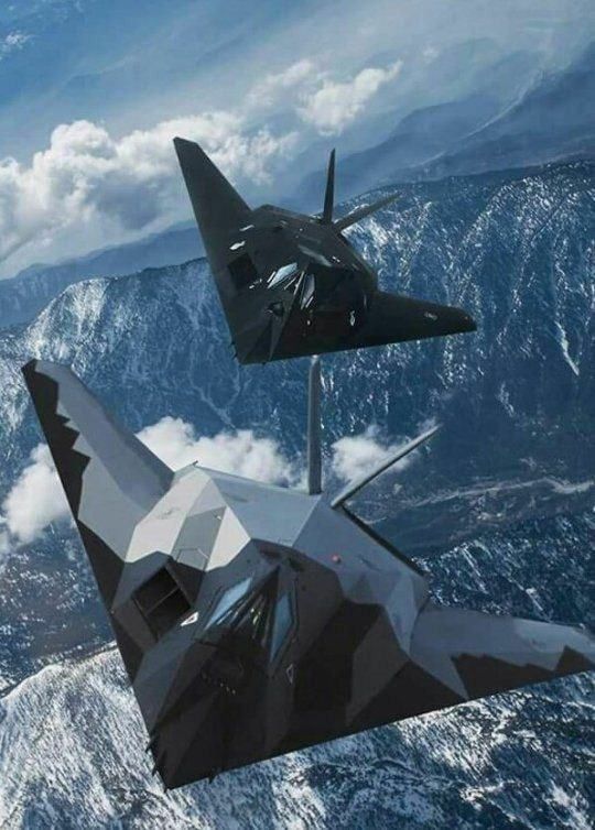 two fighter jets flying in the sky over mountains and snow covered ground, with one plane upside down