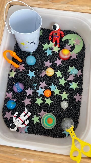 a tray filled with toys on top of a wooden table next to scissors and a cup