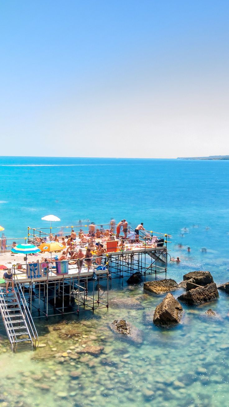 a group of people sitting on top of a pier next to the ocean with umbrellas