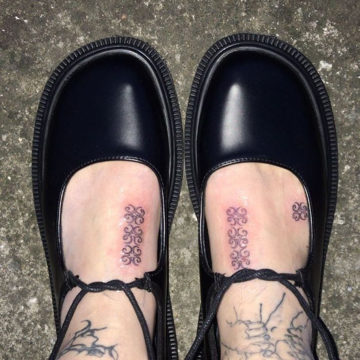 a woman's feet with tattoos on them and her shoes covered in black laces