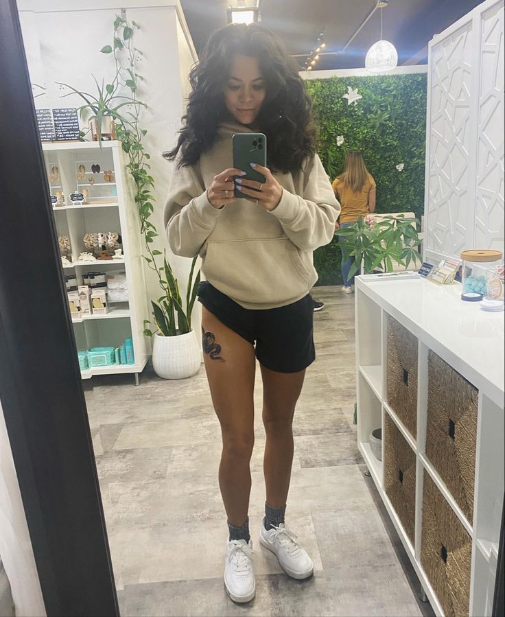 a woman standing in front of a mirror looking at her cell phone while wearing shorts