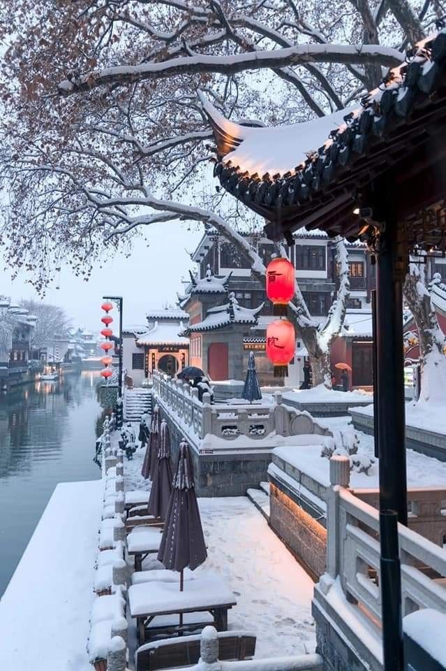 the snow covered walkway is lined with benches and umbrellas on either side of the water