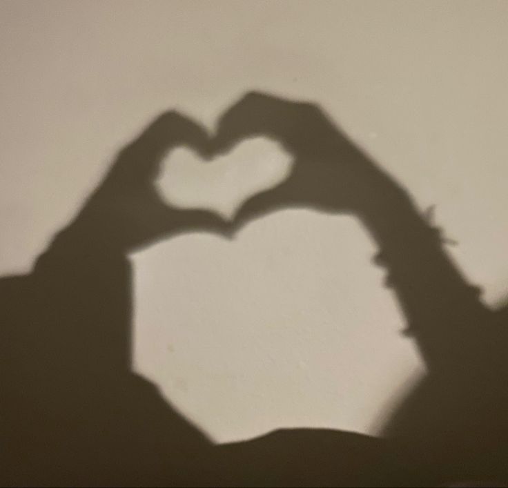 the shadow of a person making a heart with their hands in front of a wall