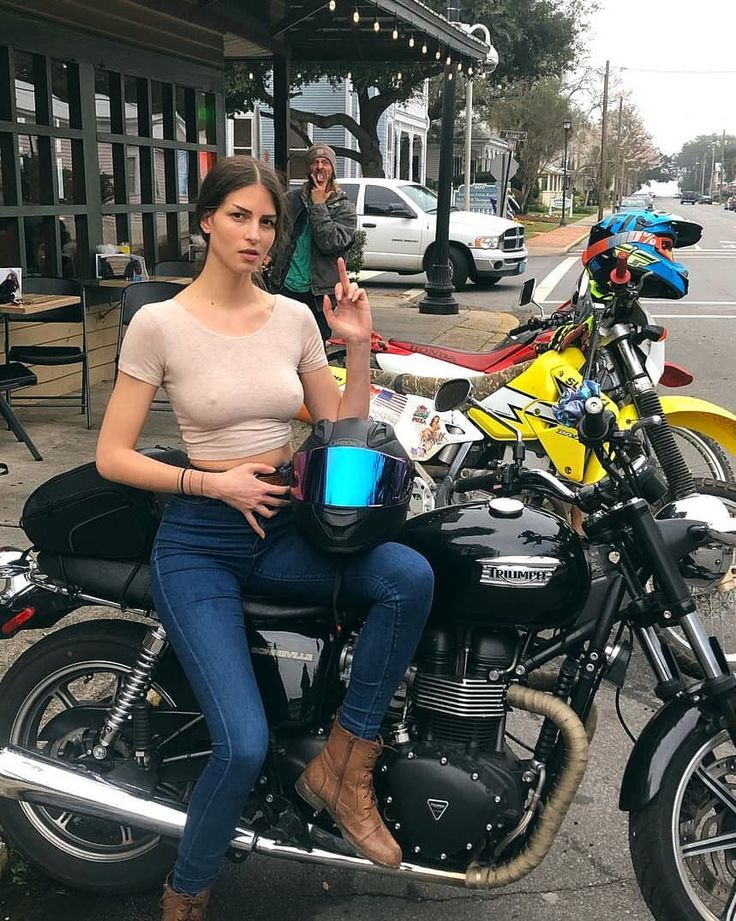 a woman sitting on top of a motorcycle with a cup in her hand and another person standing next to her