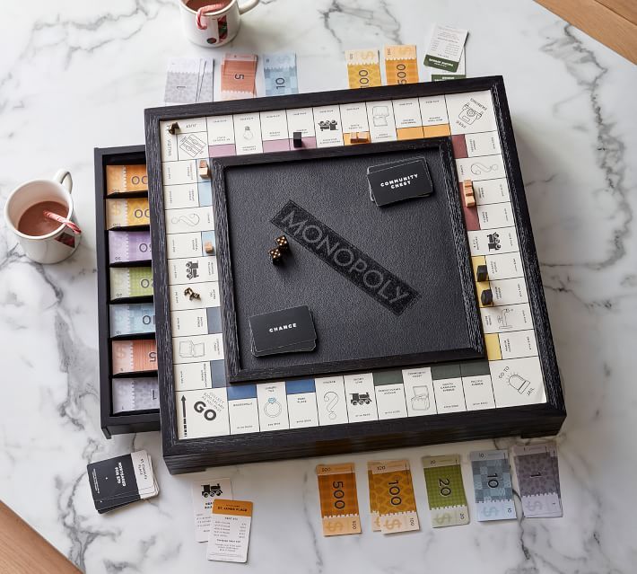 a monopoly board game on a marble table next to coffee mugs and other items