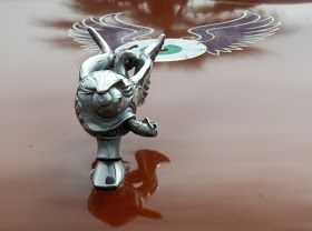 a metal object on the hood of a car that is shiny red and has winged wings