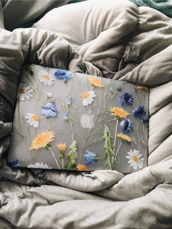 a pillow that is on top of a bed covered in blankets and pillows with flowers painted on it