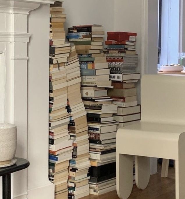 a stack of books sitting on top of a wooden floor next to a white chair