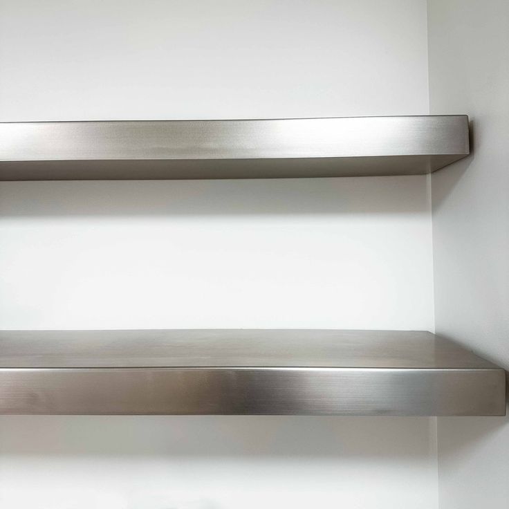 two stainless steel shelves against a white wall