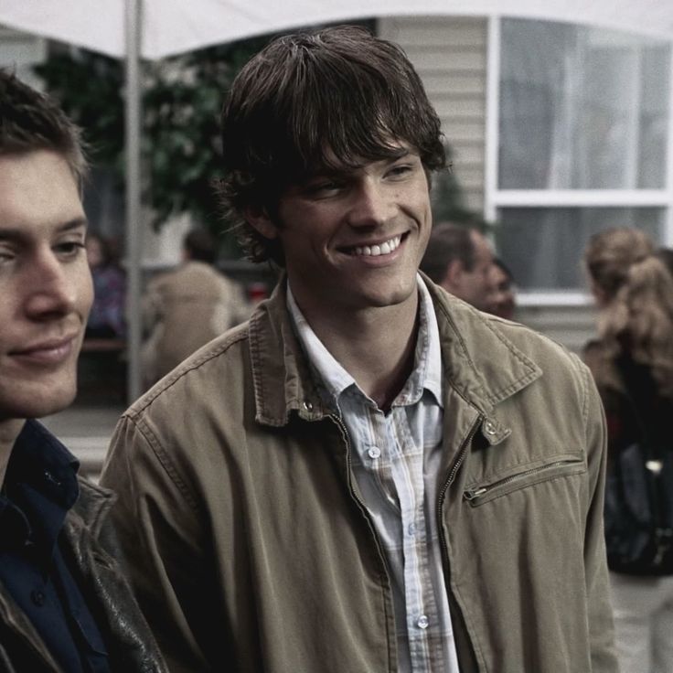 two young men standing next to each other in front of a building with lots of people