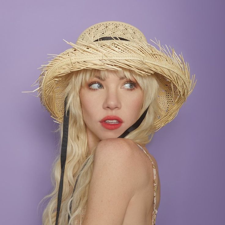 a woman wearing a straw hat with her hair in the wind and looking at the camera