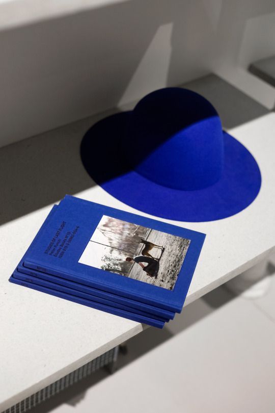 a blue hat sitting on top of a table next to a stack of photos and a book