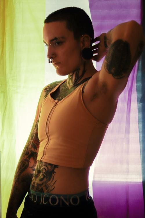 a woman with tattoos on her arm and arms is standing in front of a curtain